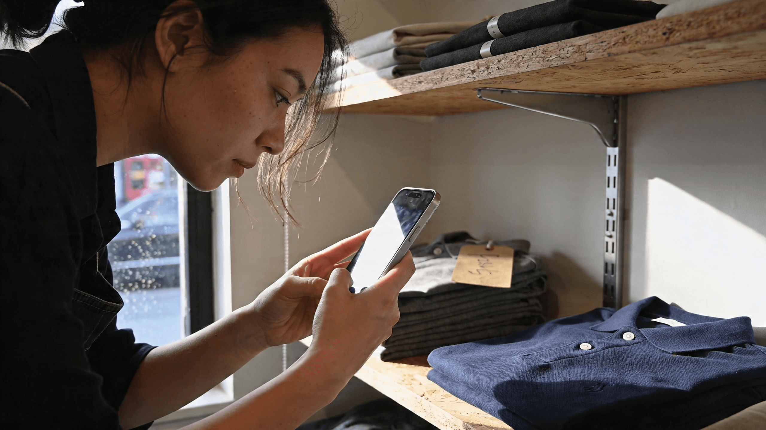 An associate photographing folded jeans on a stockroom shelf
